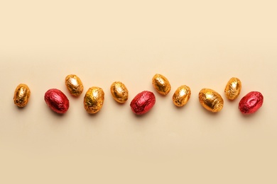 Chocolate eggs wrapped in red and golden foil on beige background, flat lay