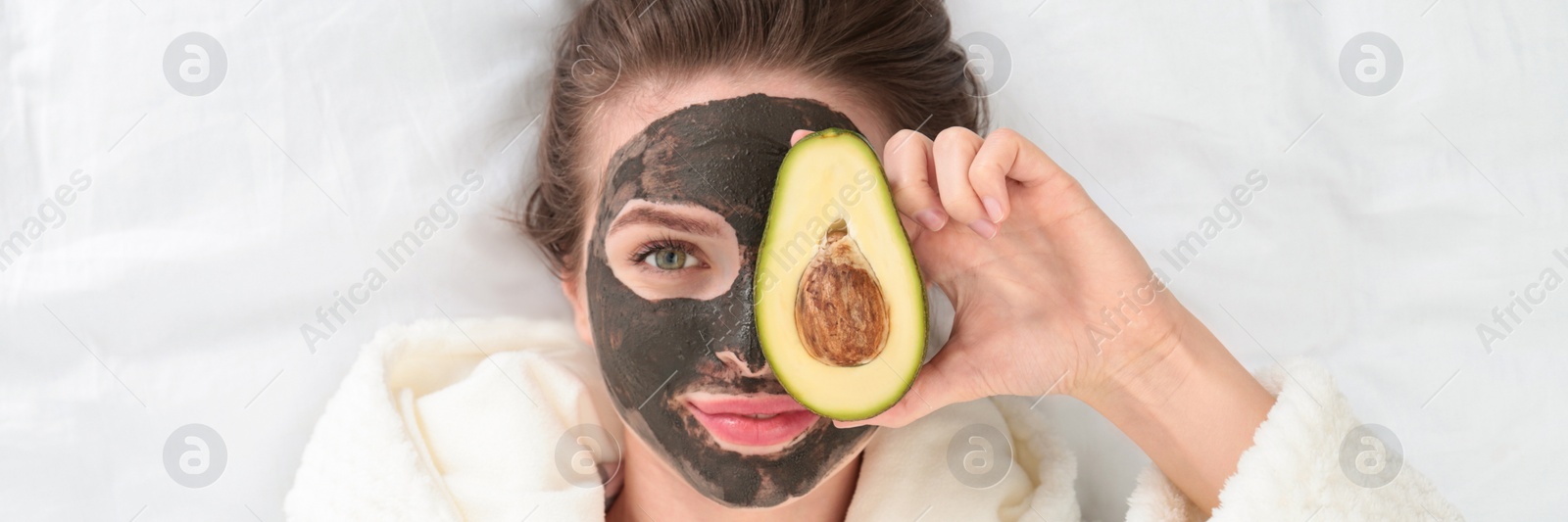 Image of Young woman with facial mask and avocado lying on bed, top view. Banner design