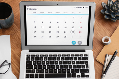 Photo of Modern laptop with calendar on wooden table, above view