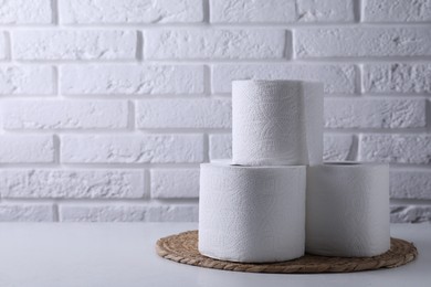 Toilet paper rolls on white table against brick wall, space for text