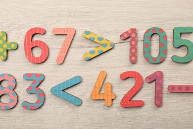 Colorful numbers and mathematical symbols on light wooden table, flat lay