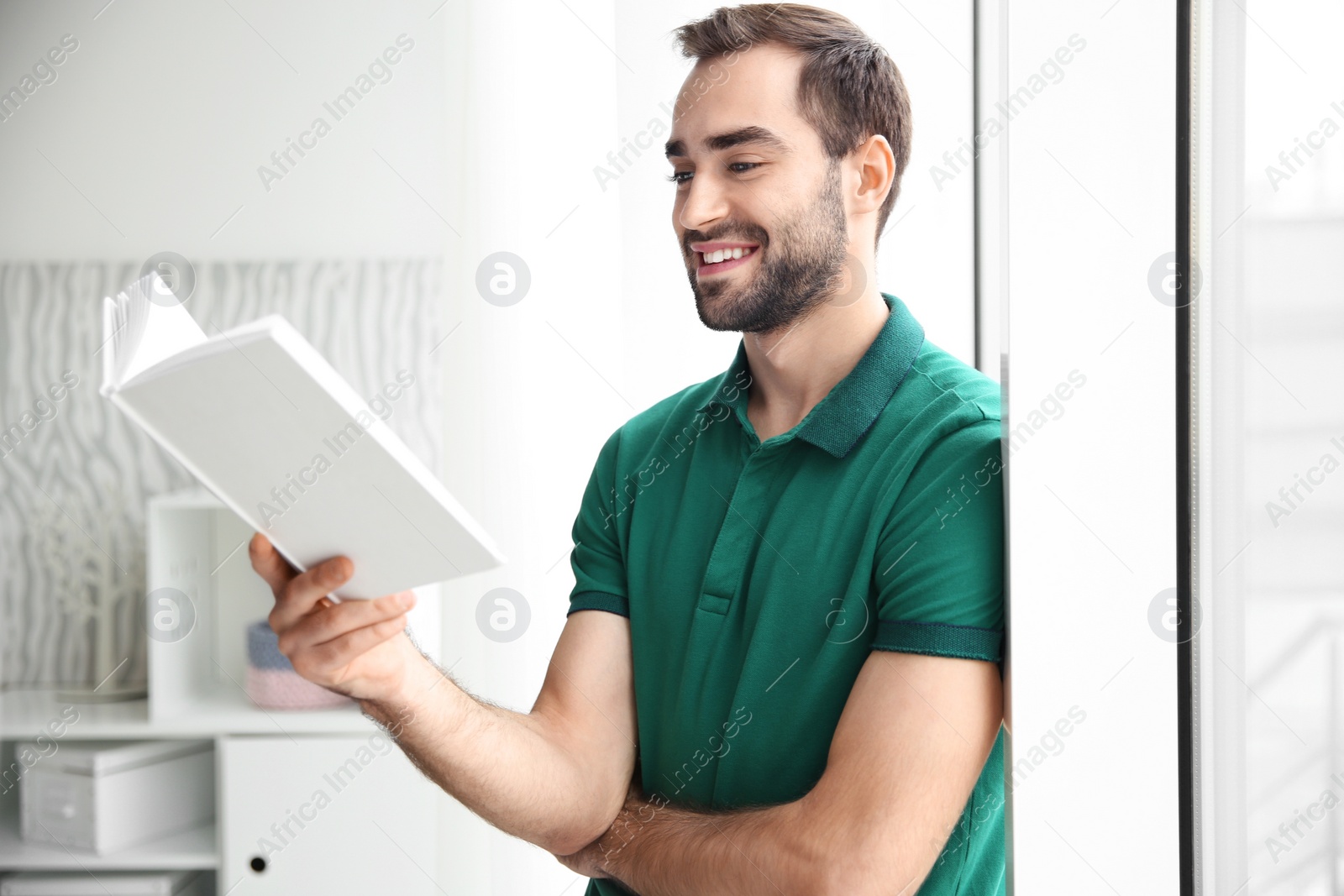 Photo of Young man reading book near window at home