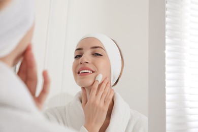 Woman using silkworm cocoon in skin care routine near mirror at home