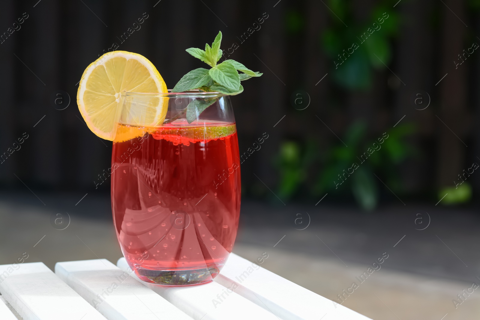 Photo of Glass of delicious cocktail on white wooden table outdoors, space for text. Refreshing drink