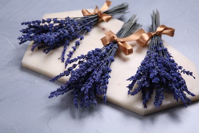 Photo of Bouquets of beautiful preserved lavender flowers and stone board on light grey textured table