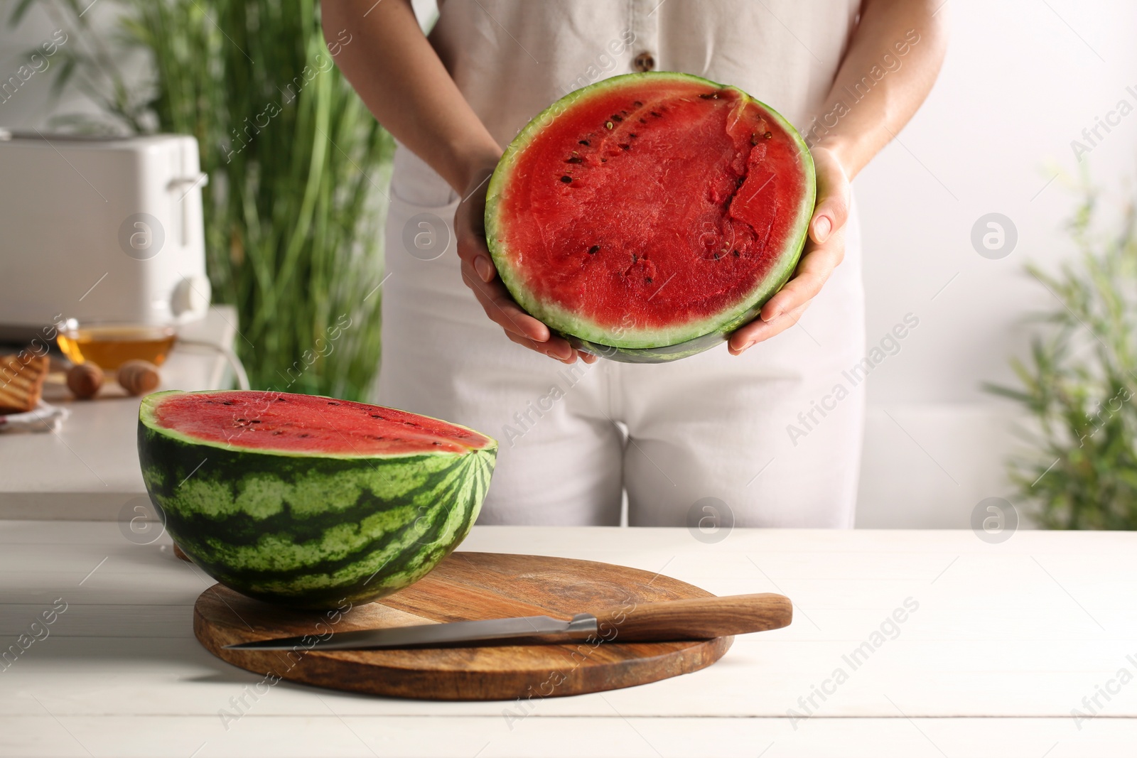 Photo of Woman with delicious cut watermelon at white wooden table in kitchen, closeup