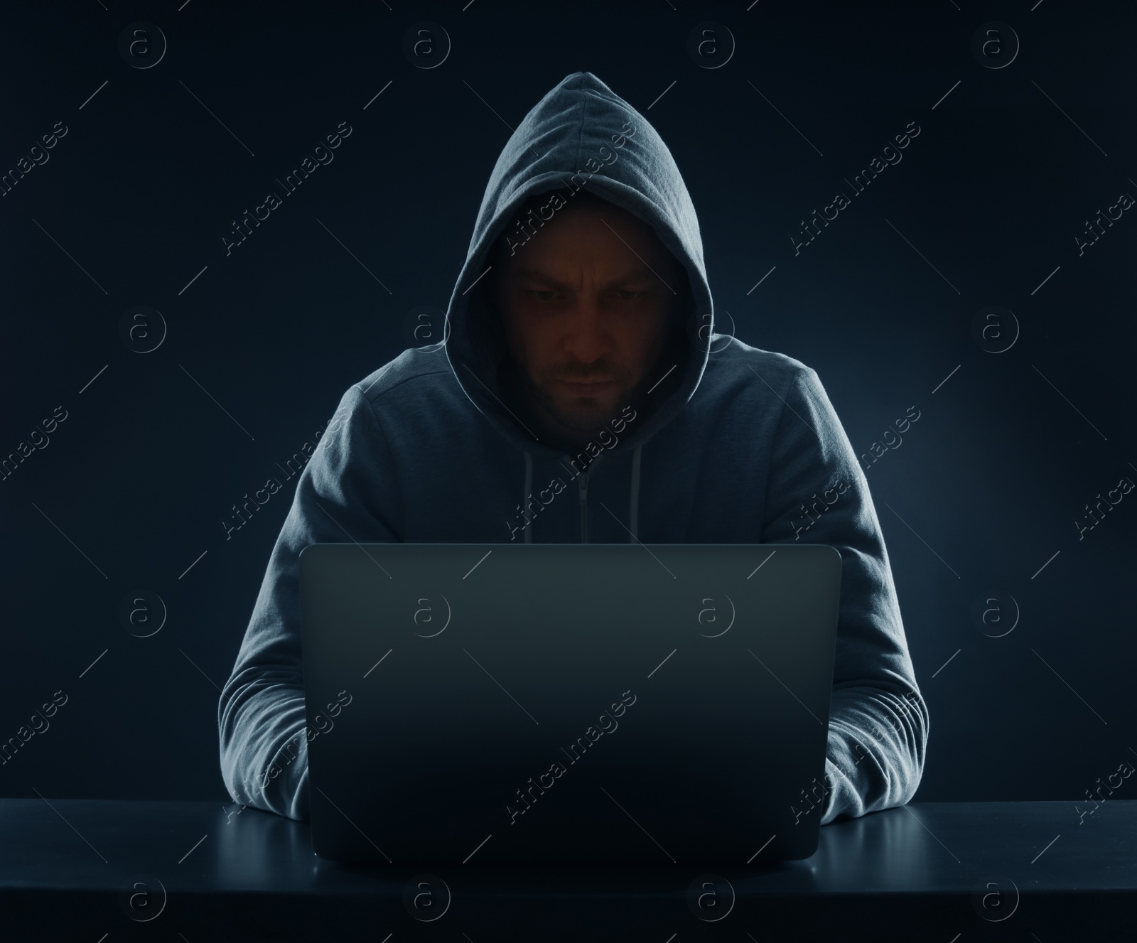 Photo of Man using laptop at table on dark background. Criminal activity