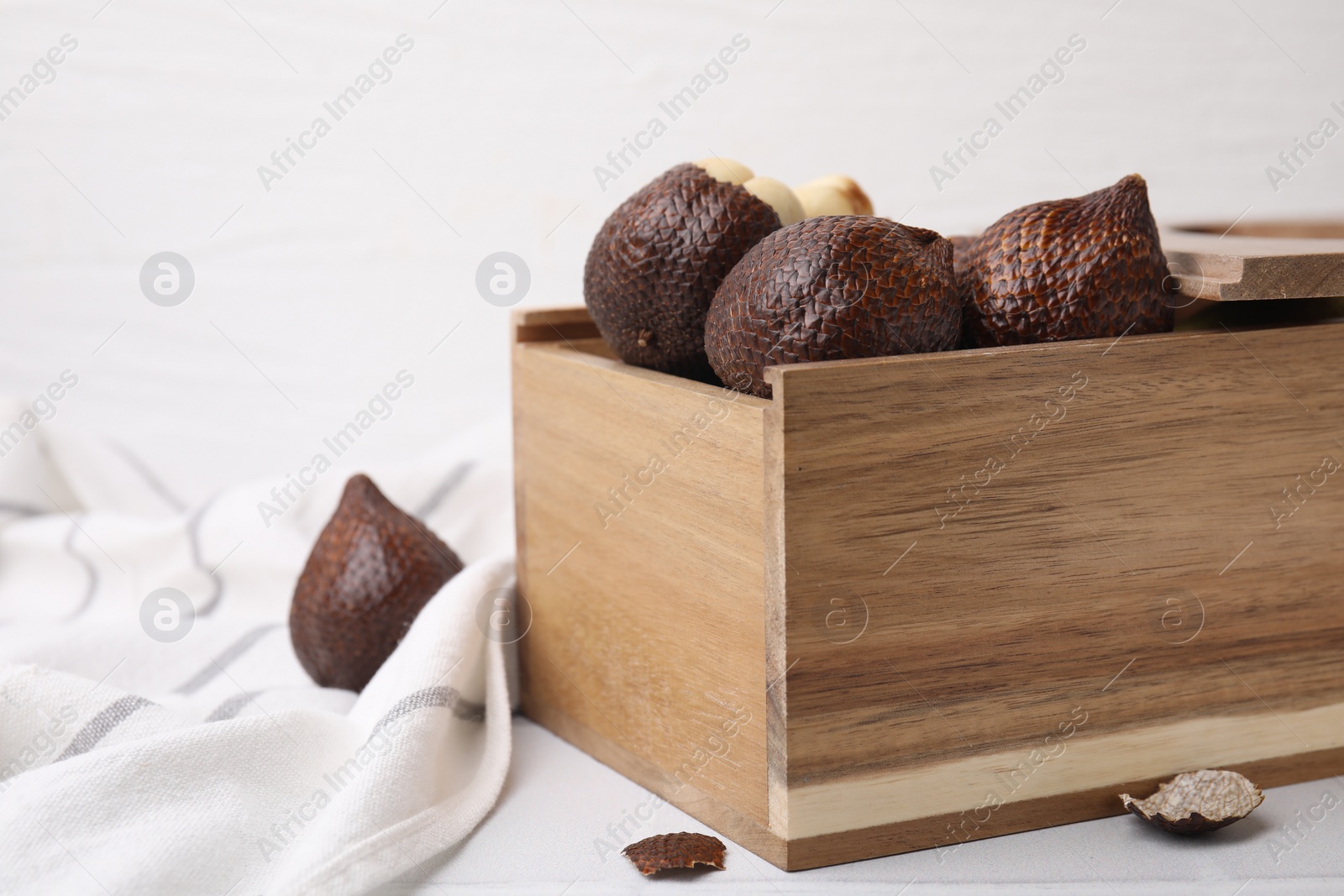 Photo of Wooden crate with fresh salak fruits on white table, closeup. Space for text