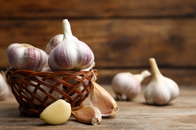 Photo of Fresh organic garlic in wicker basket on wooden table