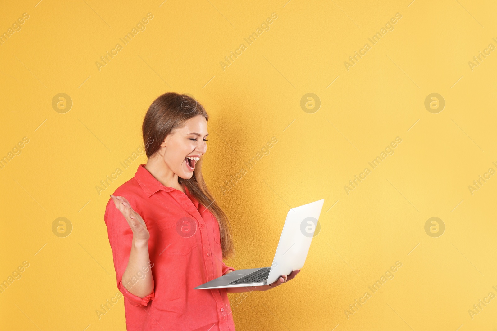 Photo of Emotional young woman with laptop celebrating victory on color background. Space for text