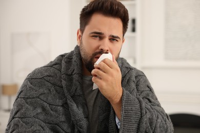 Photo of Sick man wrapped in blanket with tissue at home. Cold symptoms