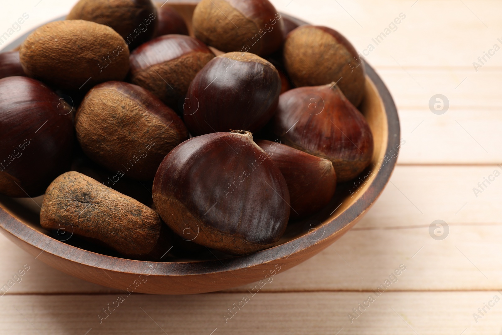 Photo of Sweet fresh edible chestnuts on light wooden table, closeup