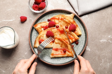 Woman eating delicious thin pancakes with syrup and berries at table, top view