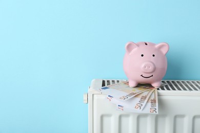 Photo of Piggy bank and euro banknotes on heating radiator against light blue background, space for text