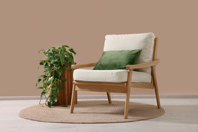 Photo of Stylish armchair with cushion and green plant near beige wall indoors