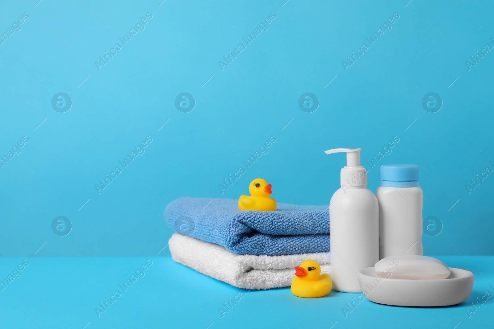 Photo of Baby cosmetic products, bath ducks and towels on light blue background. Space for text