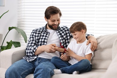 Photo of Happy Father's day. Son giving gift box to his dad on sofa at home