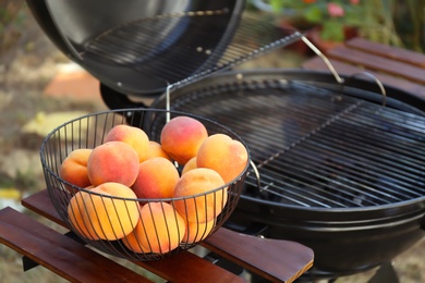 Photo of Fresh peaches on wooden table near modern grill outdoors