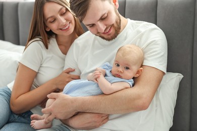 Photo of Happy family. Parents with their cute baby on bed indoors