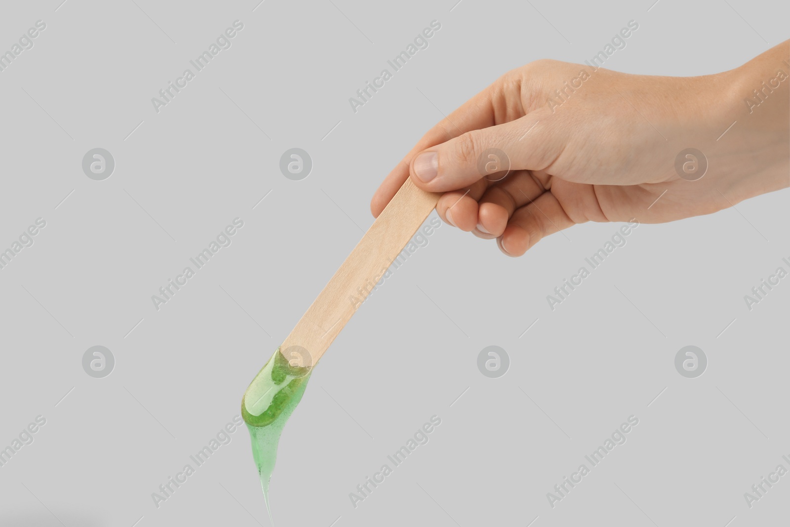 Photo of Woman holding spatula with hot depilatory wax on light  background, closeup