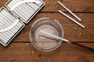 Photo of Cigarettes, holder, case and ashtray on wooden table, flat lay