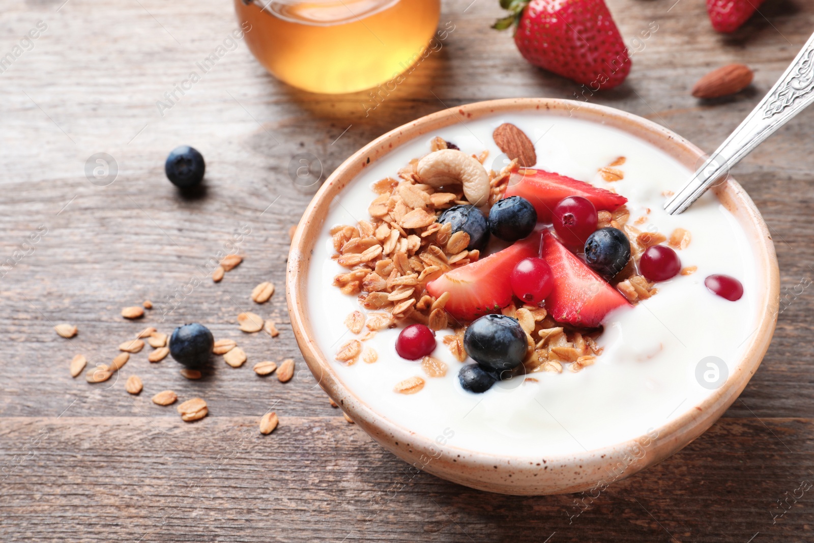 Photo of Bowl with yogurt, berries and granola on wooden table