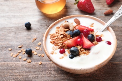 Photo of Bowl with yogurt, berries and granola on wooden table
