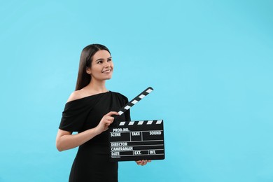 Photo of Happy actress with clapperboard on light blue background, space for text. Film industry