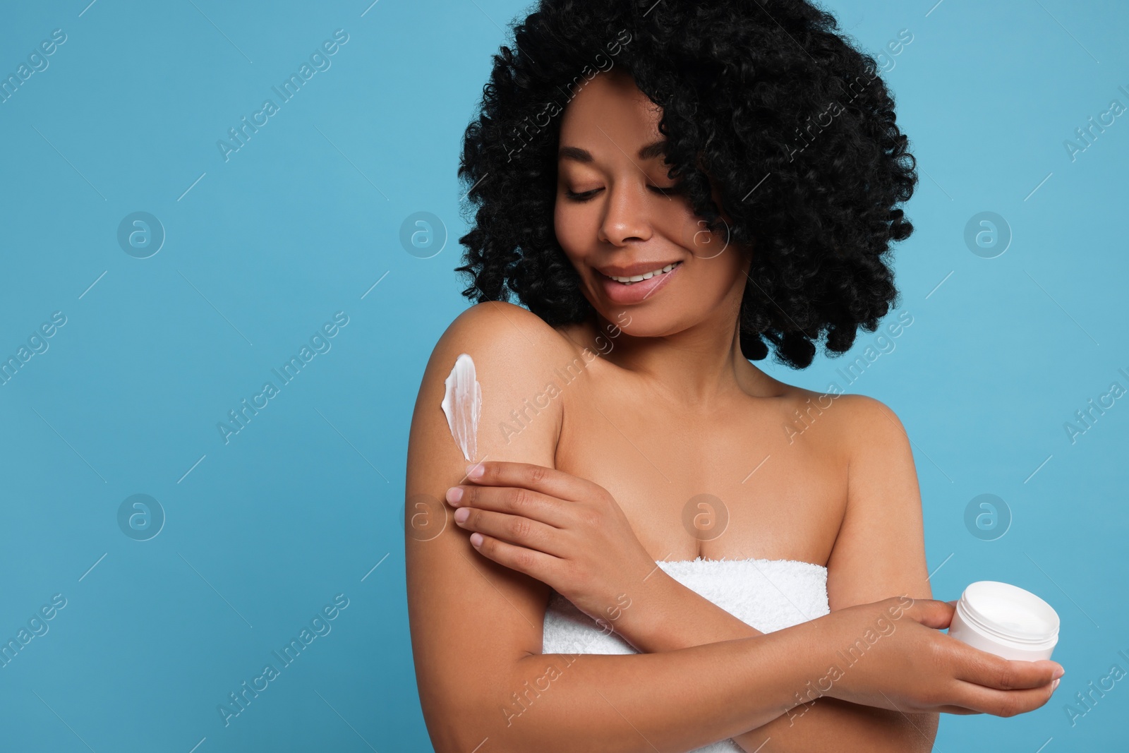 Photo of Young woman applying body cream onto shoulder on light blue background. Space for text