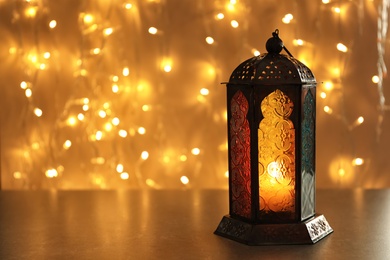Muslim lamp with candle on table against blurred fairy lights. Fanous as Ramadan symbol