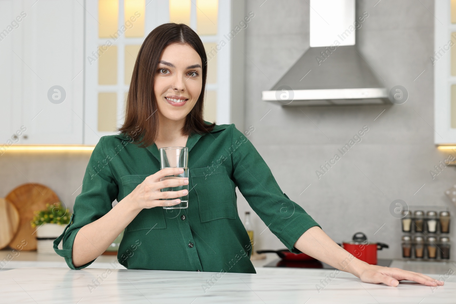 Photo of Young woman holding glass with clean water in kitchen