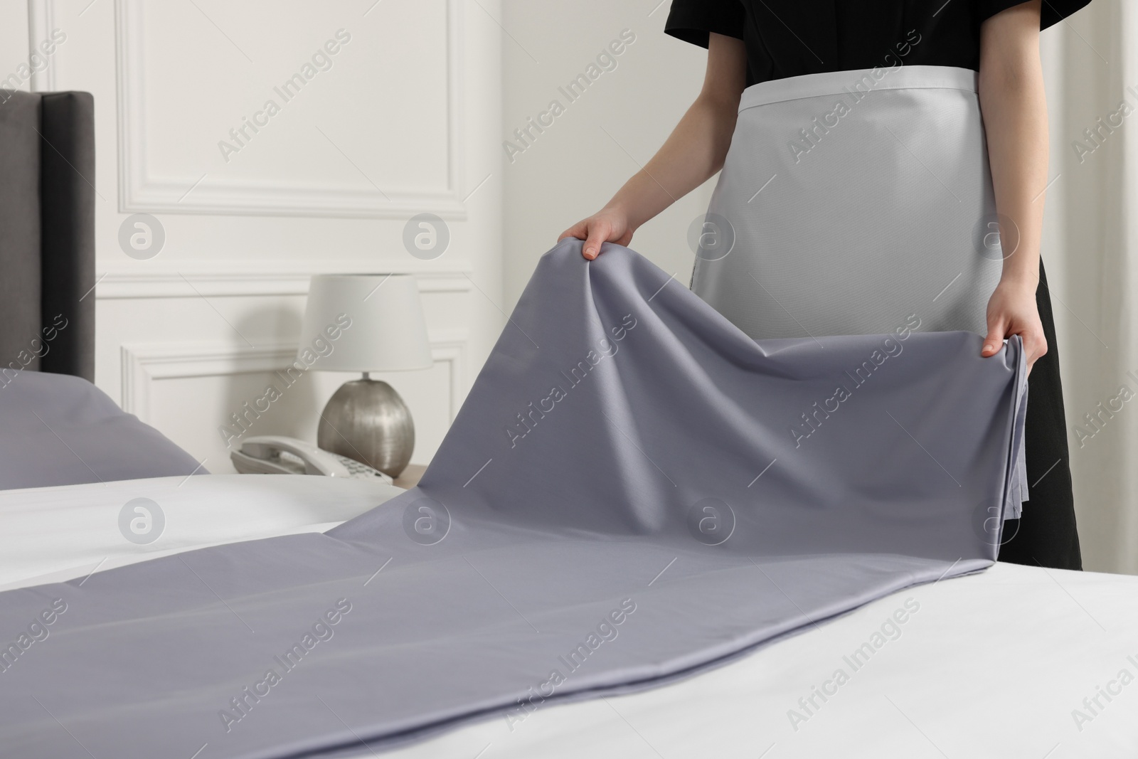 Photo of Young maid making bed in hotel room, closeup