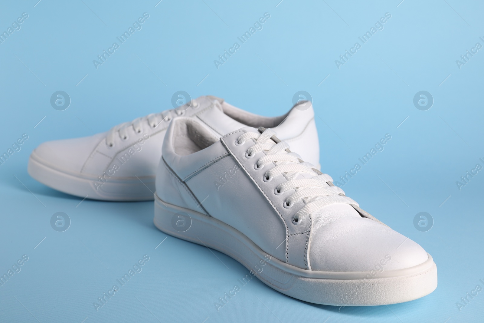 Photo of Pair of stylish white sneakers on light blue background