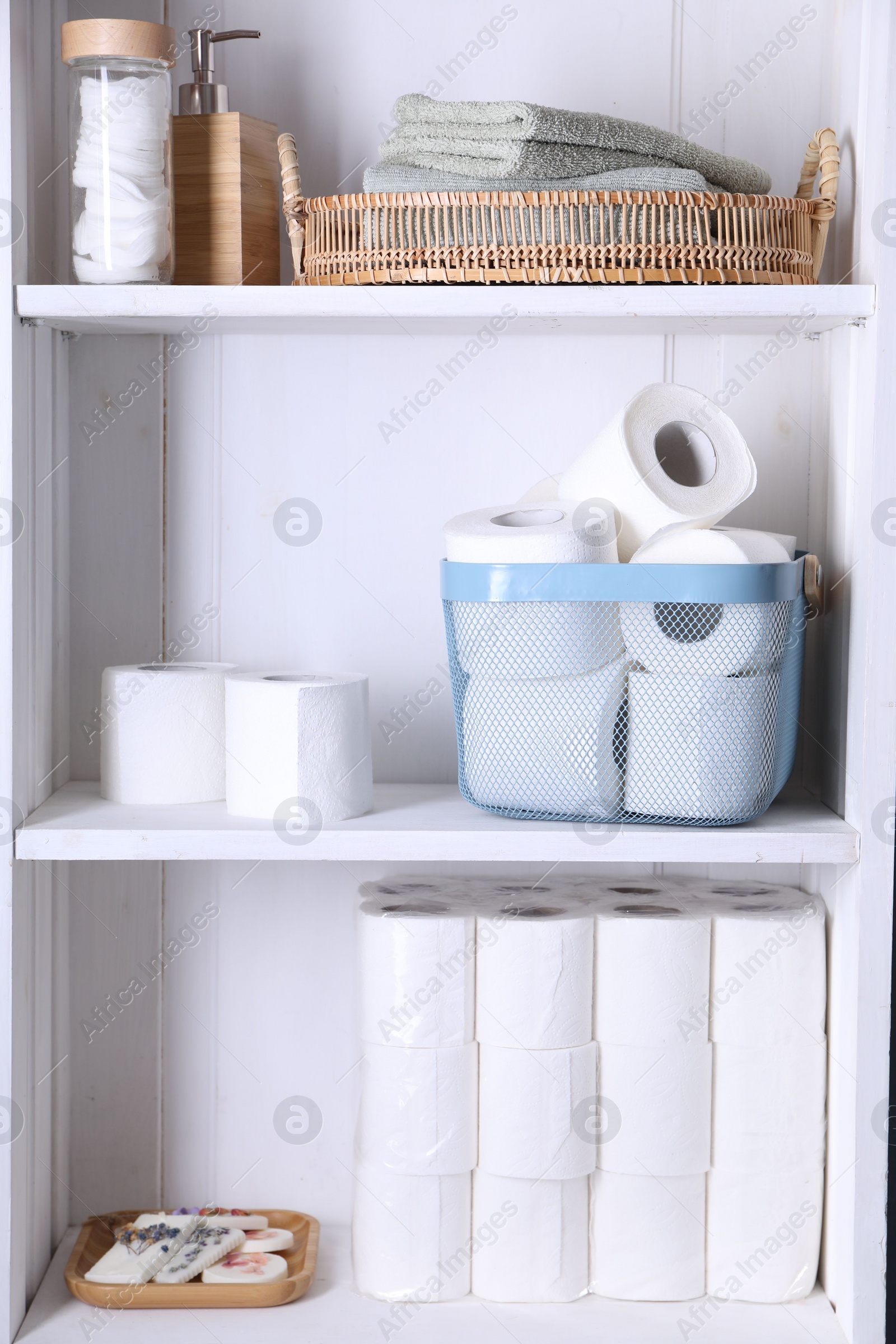 Photo of Toilet paper rolls, soap, cotton pads and towels on white shelves