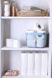 Toilet paper rolls, soap, cotton pads and towels on white shelves