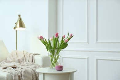 Photo of Beautiful tulips and burning candle on white table indoors. Interior design
