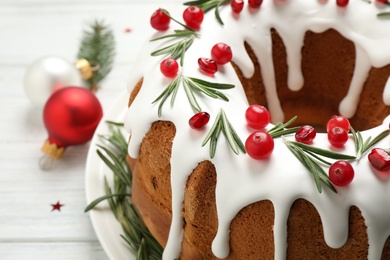 Photo of Traditional Christmas cake decorated with glaze, pomegranate seeds, cranberries and rosemary on white table, closeup