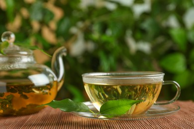 Photo of Fresh green tea in glass cup, teapot and leaves on bamboo mat
