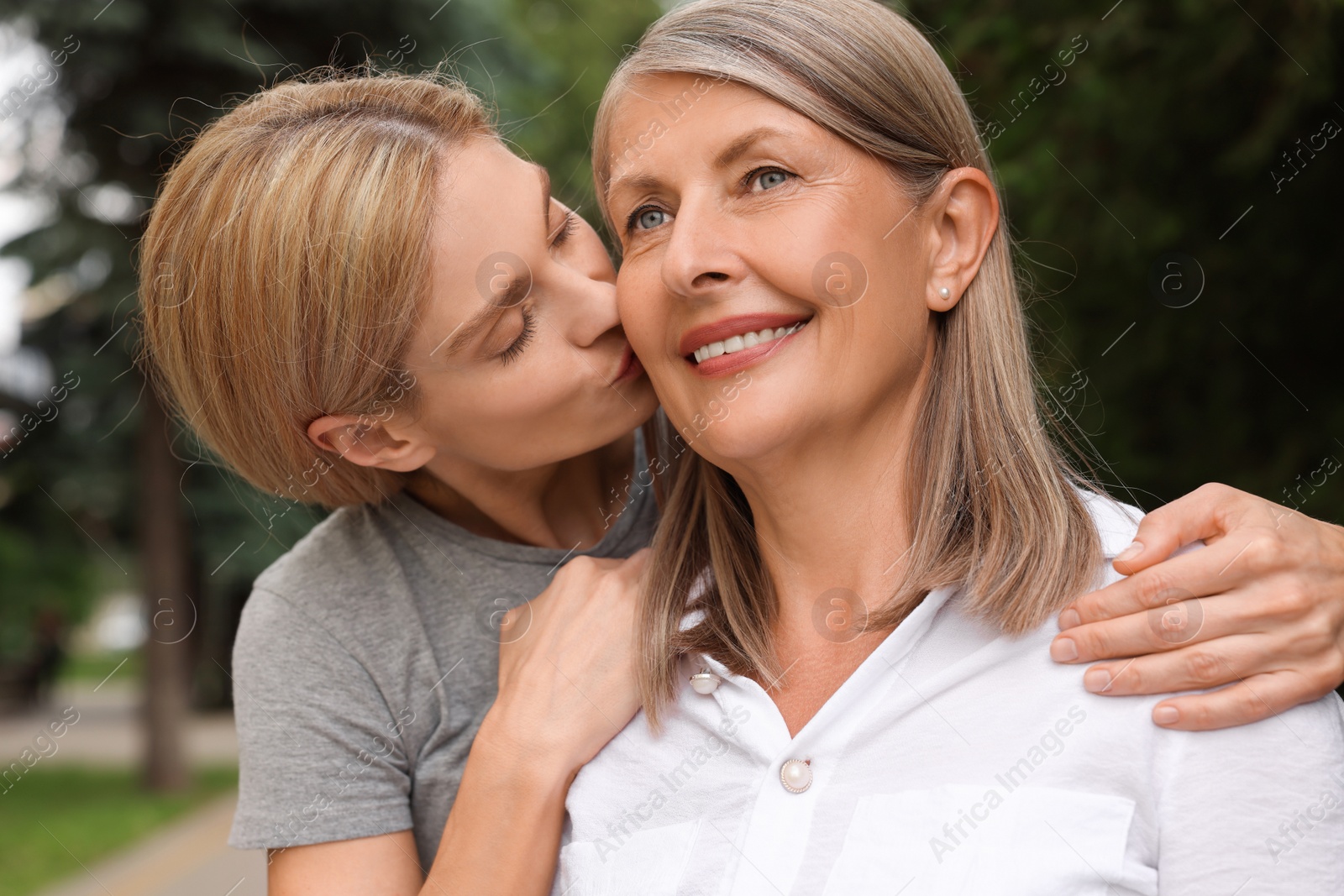 Photo of Daughter kissing her mature mother on cheek outdoors