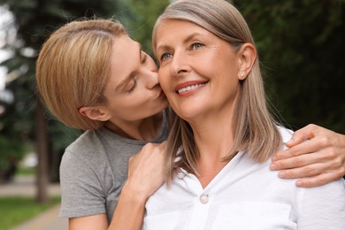 Photo of Daughter kissing her mature mother on cheek outdoors