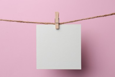 Photo of Wooden clothespin with blank notepaper on twine against pink background. Space for text