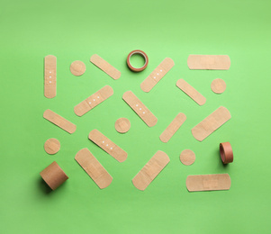 Different types of sticking plasters on green background, flat lay