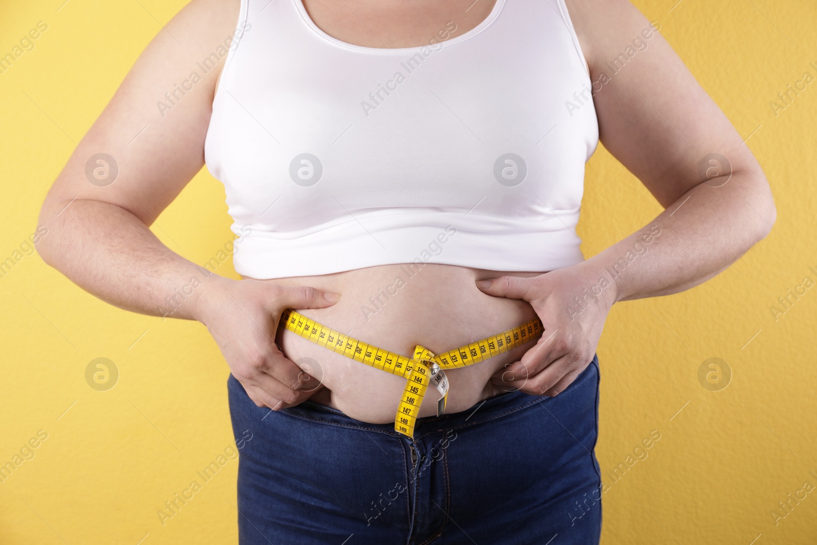 Photo of Overweight woman measuring waist with tape on color background, closeup