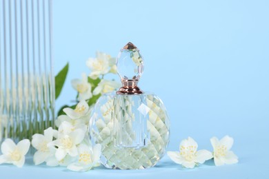 Aromatic perfume in bottle and beautiful jasmine flowers on light blue background, closeup. Space for text