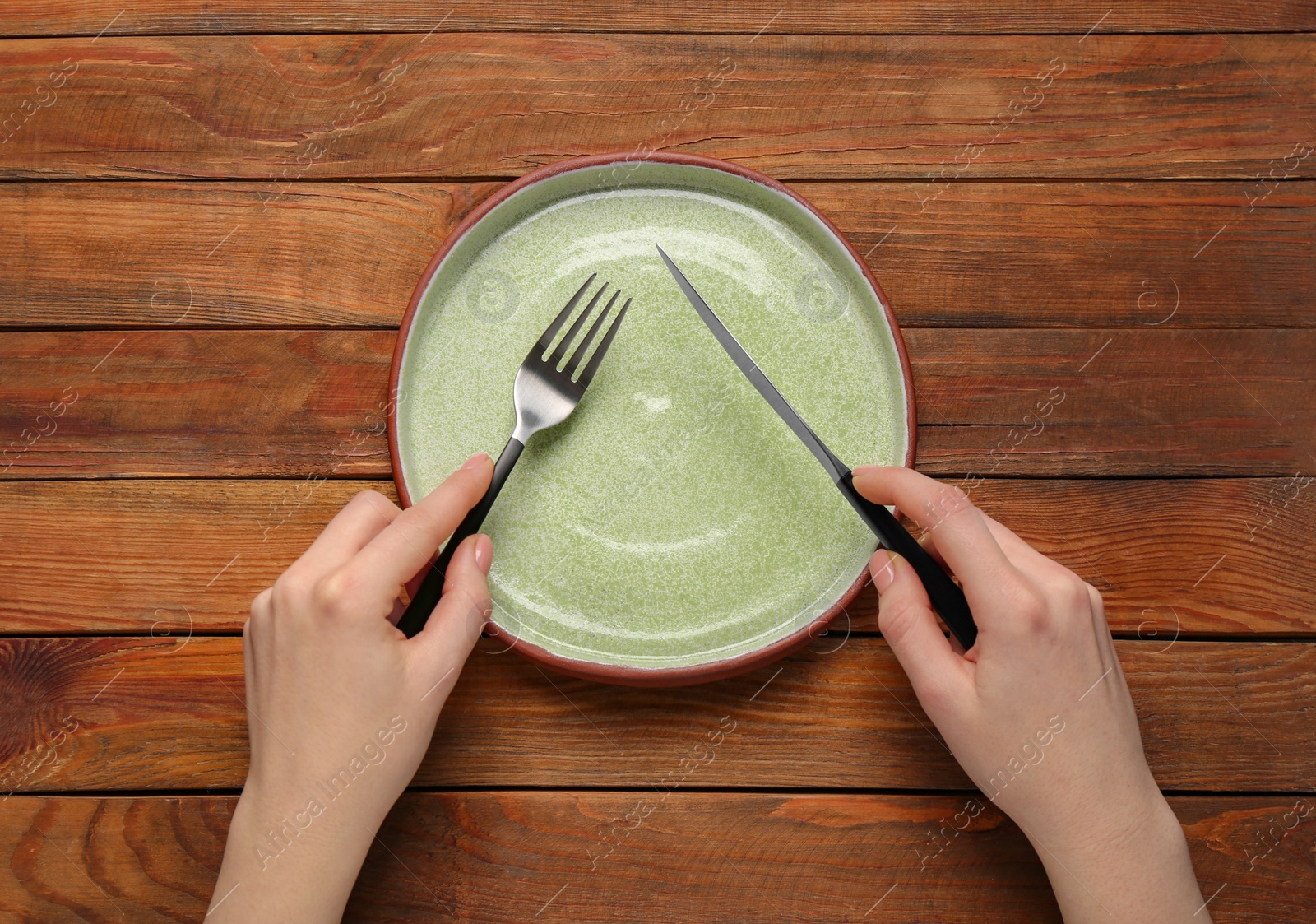Photo of Woman with empty plate and cutlery at wooden table, top view
