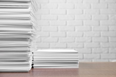 Stacks of paper sheets on wooden table near white brick wall, space for text