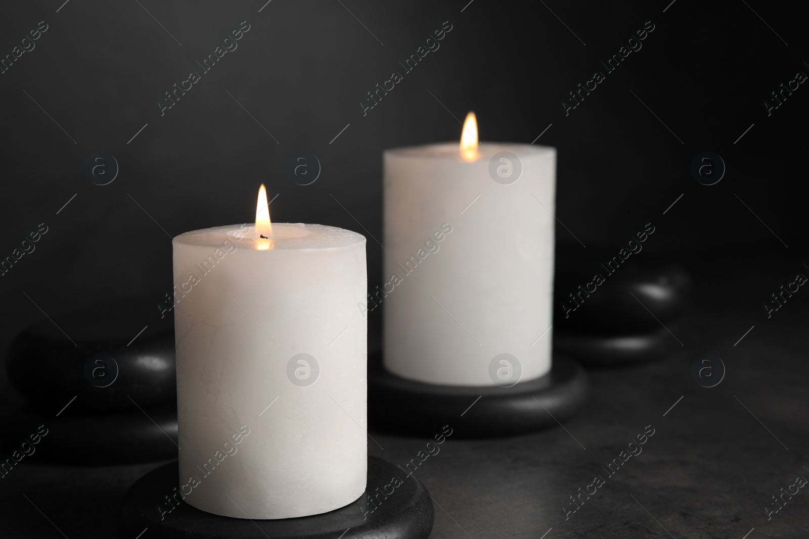 Photo of Burning candles and black spa stones on grey table