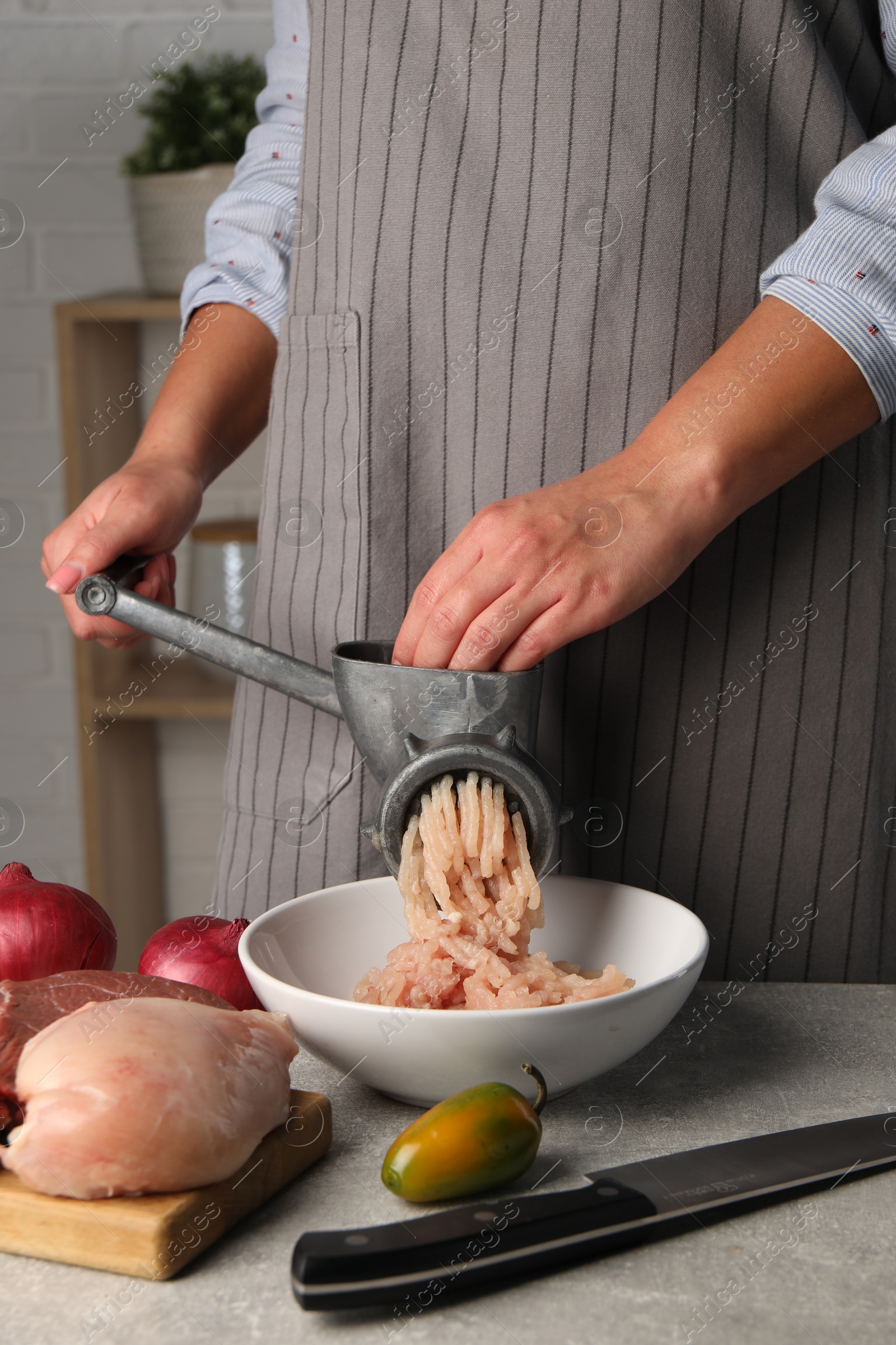 Photo of Woman making chicken mince with metal meat grinder at grey table indoors, closeup