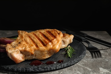 Photo of Grilled meat served with rosemary and sauce on slate plate against black background. Space for text