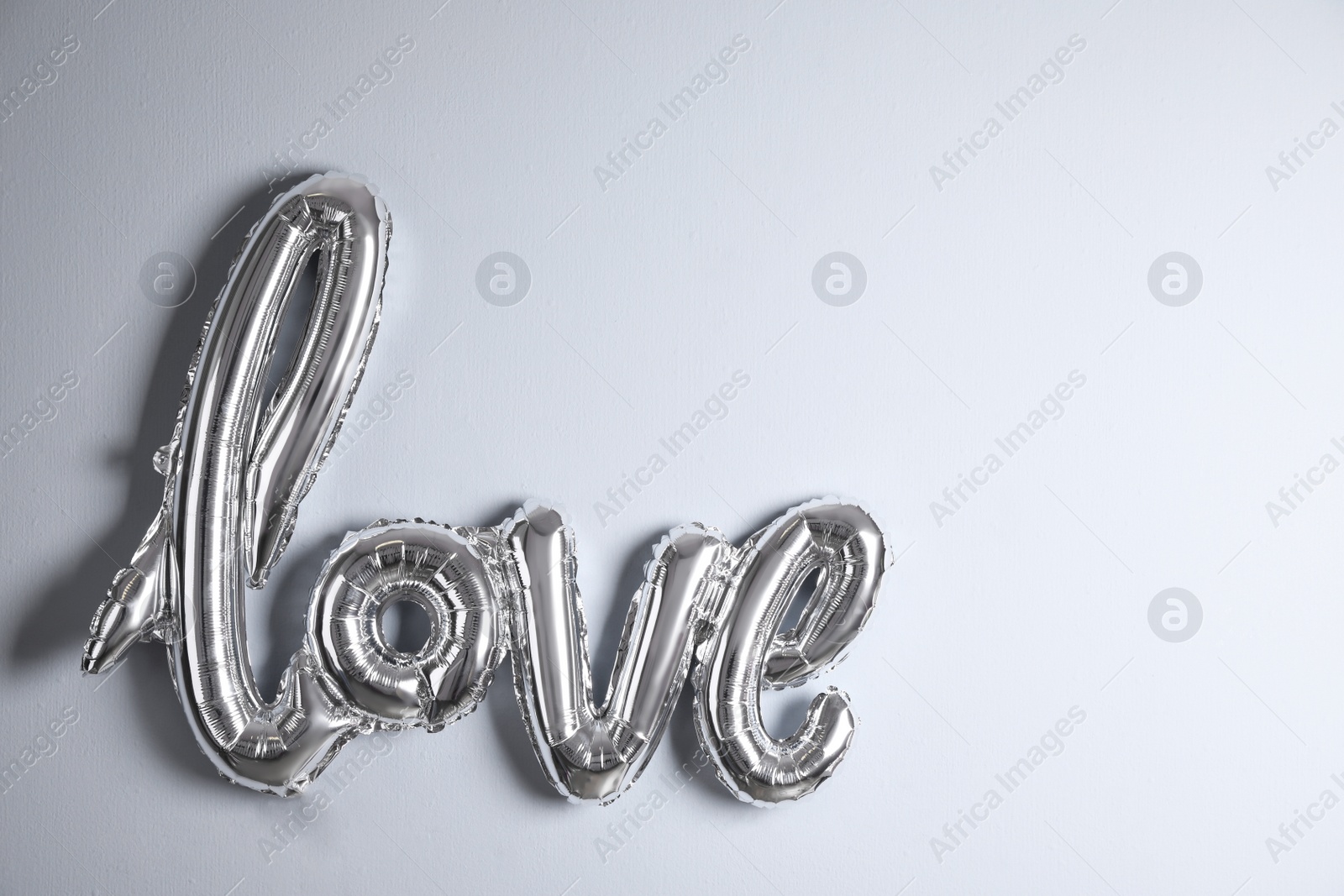 Photo of Silver balloon in shape of word LOVE near light wall